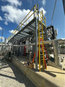 Galvanized steel catwalk platform with yellow OSHA-compliant guardrails and ladder access, installed above industrial equipment at a wastewater treatment plant.